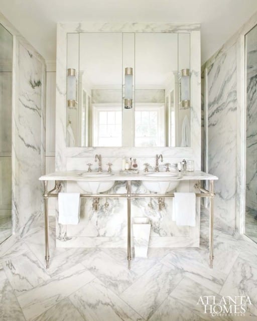 Marble bathroom with a double vanity featuring undermount sinks, polished nickel fixtures, and a mirrored medicine cabinet. The floor is laid in a herringbone pattern of marble tiles.