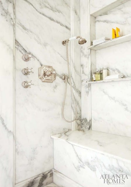 Marble shower with polished nickel fixtures, built-in bench, and recessed shelves holding toiletries and towels.