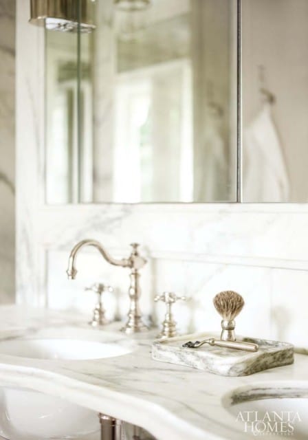 Marble bathroom vanity with double sinks, a chrome faucet, and a marble tray holding a shaving brush and razor.