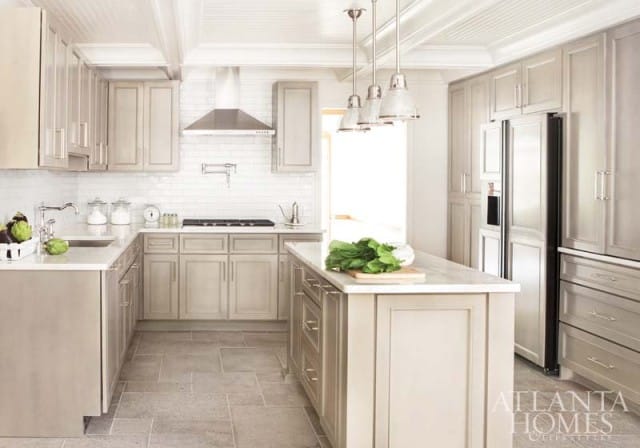 Neutral kitchen with light gray cabinetry, white subway tile backsplash, stainless steel appliances, and a marble-topped island with greens.