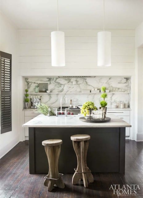 Modern kitchen with dark gray island, white marble countertops, marble backsplash, and two white cylindrical pendant lights.