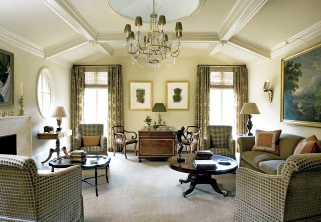 Living room with coffered ceiling, ornate chandelier, patterned drapes, two armchairs, a sofa, and a desk with artwork above.