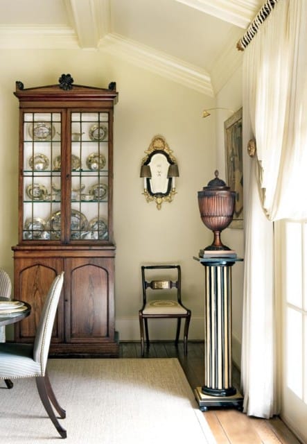 Dining room with a tall wooden china cabinet filled with plates, a small antique chair, and a decorative urn on a fluted pedestal.