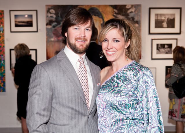 A man in a grey pinstripe suit and pink striped tie stands next to a woman in a one-shoulder dress with a swirling pattern of green, purple, and white.