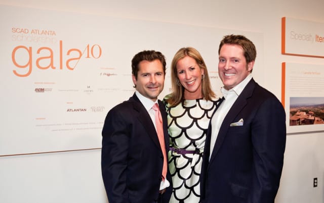 Three people pose for a photo in front of a wall displaying SCAD Atlanta Scholarship Gala 2010 sponsors and information.