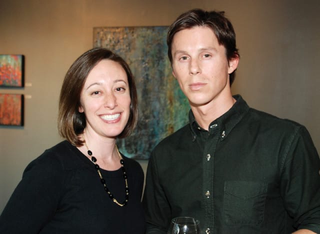 Woman with short brown hair wearing a black top and beaded necklace smiles next to a man in a dark green button-down shirt.