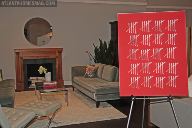 Living room with a wooden fireplace, round mirror, green sofa, chaise lounge, and a red easel displaying tally marks.