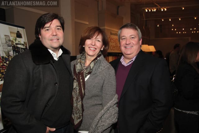 Three people smiling at the camera. The person on the left wears a dark coat with a fur collar. The person in the middle wears a gray sweater and patterned scarf. The person on the right wears a dark suit jacket over a purple sweater.