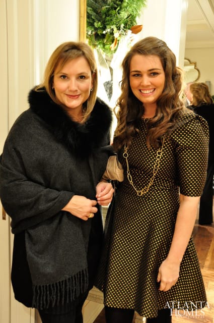 Janie Wilburn and Whitney Ray smile for a photo. Wilburn wears a dark grey shawl with a fur collar, and Ray wears a black and gold polka dot dress with a gold chain necklace.