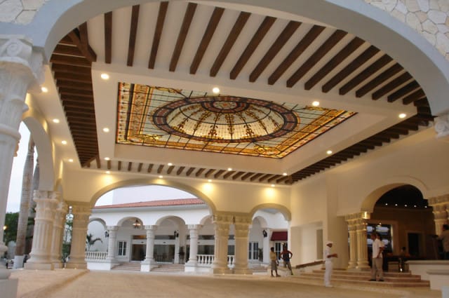 Grand hotel lobby with a large stained-glass dome ceiling, white columns, arched doorways, and exposed wooden beams.