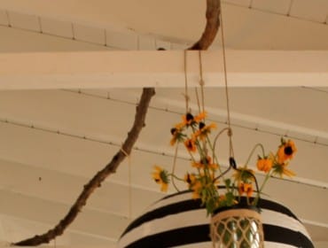 Black and white striped paper lanterns hang from a porch ceiling, adorned with woven baskets holding yellow flowers.