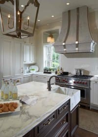 White kitchen with marble island and countertops, dark wood cabinetry, stainless steel range, and ornate lantern pendant light.