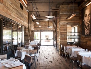 Restaurant interior with reclaimed wood walls, white tablecloths, and a large black and white portrait of a woman smoking.