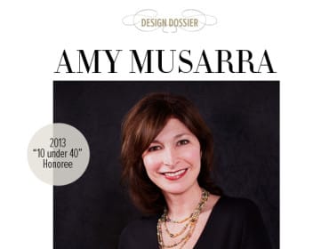 Amy Musarra smiling, wearing a black top and beaded necklace, with a dark background. Text reads "2013 '10 under 40' Honoree" and "DESIGN DOSSIER"