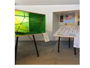Two display cases on black legs, one with a green interior and black string art, the other with rows of small white objects and vintage posters.