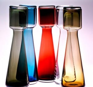 Group of five colorful glass decanters in various shades of green, blue, red, clear, and amber, with metallic tops.
