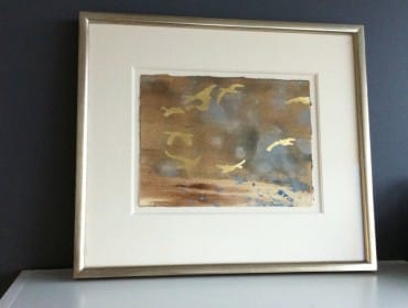 Framed watercolor painting of birds in flight with gold leaf accents against a muted brown and grey background.