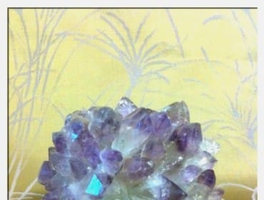 Cluster of purple and clear amethyst crystals with iridescent blue highlights, resting on a textured yellow fabric with a white abstract branch pattern.