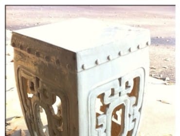 White ceramic garden stool with intricate lattice cutouts and decorative studs along the top edge, resting on a concrete surface with fallen leaves.