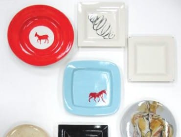 Collection of decorative plates including a red plate with a horse, a blue plate with a horse, a black square plate, and various other plates with abstract designs and illustrations.