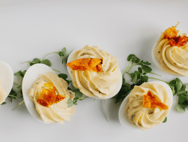 Deviled eggs topped with creamy yellow filling, garnished with crispy orange pieces and microgreens on a white platter