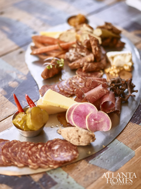 Charcuterie board with sliced salami, prosciutto, cheese, pickles, radishes, and bread on a metal platter