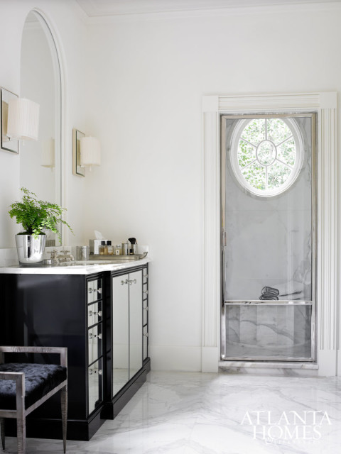 White bathroom with a black vanity featuring mirrored cabinet doors, a marble countertop, and a chrome-framed oval shower with a window view.