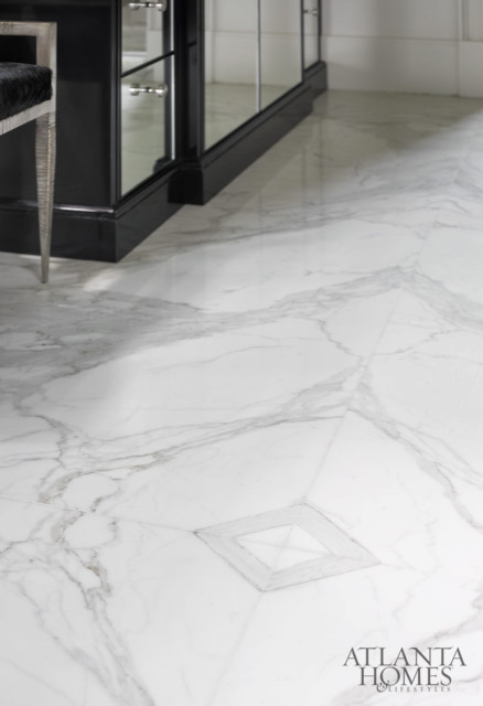 White marble flooring with gray veining and a geometric inlay detail. A black mirrored cabinet and a silver-legged chair with black upholstery are partially visible.