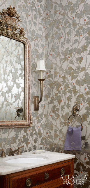 The powder room received a glamorous makeover with its Osborne & Little wallpaper in metallic silver and gold with a touch of the melon color pulled from the living room. An antique commode was retrofitted for the vanity, and the ornate mirror is from Parc Monceau.