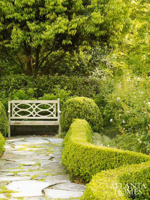 Landscape architect Joe Gayle created a series of distinct spaces, including this lined pathway that culminates with a bench overlooking climbing roses in bloom.