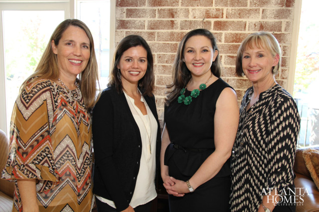 Four women smiling in front of a brick wall.