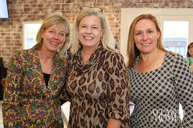 Three women smiling at the camera. The woman on the left wears a colorful paisley jacket, the woman in the middle wears a leopard print dress, and the woman on the right wears a black and white geometric print dress.
