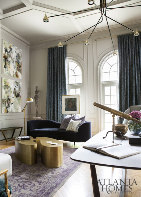 Living room with navy chaise sofa, abstract art, brass sculptural coffee tables, and a vintage telescope on a desk.