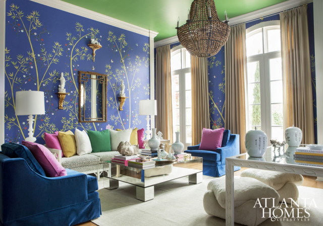 Living room with blue Chinoiserie wallpaper, green ceiling, and plush blue velvet seating. A mirrored coffee table holds decorative objects and books.