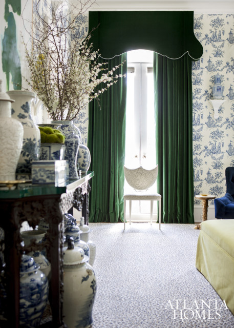Elegant living room with blue and white Chinoiserie wallpaper, deep green velvet curtains, and a collection of blue and white porcelain vases on a dark wood console table.