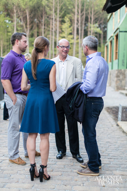 Four people in casual attire converse outdoors on a cobblestone path, with a green building and trees in the background. The Atlanta Homes & Lifestyles logo is visible in the lower right corner.