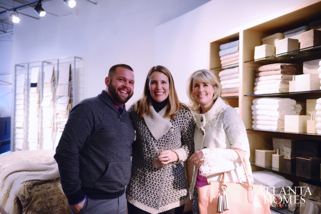 Three people smiling in a store with shelves of folded towels and linens in the background.