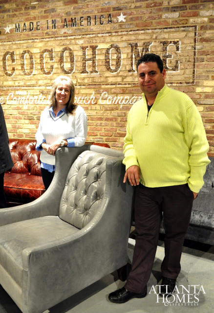 Man and woman standing in front of a brick wall with 'COCOHOME' painted on it. They are next to a tufted gray armchair and a brown leather sofa.