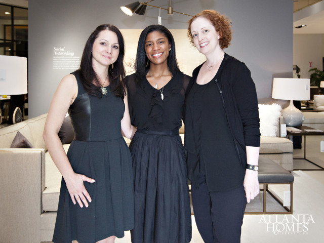 Three women in black dresses stand in a showroom with sofas and lamps in the background.