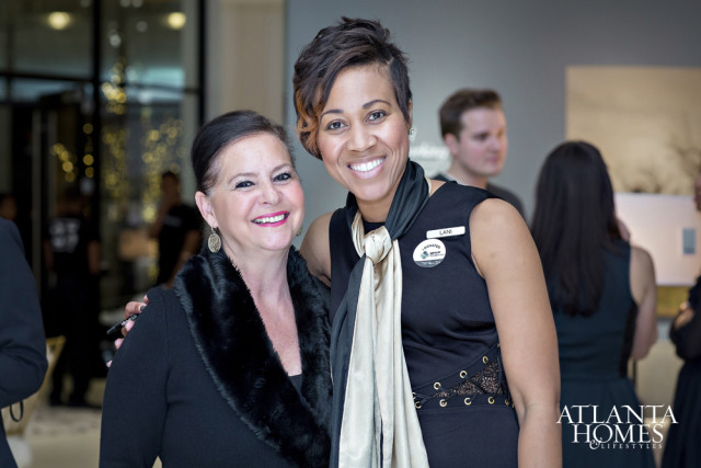 Two women smiling at the camera, one wearing a black sweater with a fur collar and the other wearing a black dress with a scarf and name tag that reads 'LANI'.