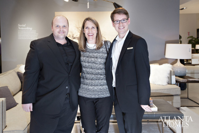 Three people posing for a photo in a showroom with furniture. The person on the right wears a name tag that reads 'JOHN'.