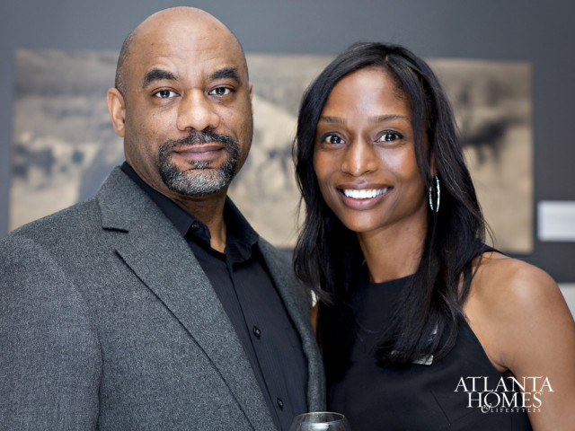 Man in a grey suit jacket and black shirt, and a woman in a black dress, pose for a portrait. The Atlanta Homes & Lifestyles logo is visible in the lower right corner.
