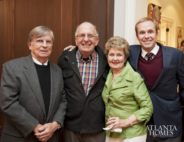 Four people posing for a photo indoors. An older man on the left wears a gray suit jacket over a black sweater. Next to him, a man in a plaid shirt and dark jacket smiles. A woman in a lime green jacket holds a drink. On the right, a man in a navy suit jacket and maroon v-neck sweater smiles.