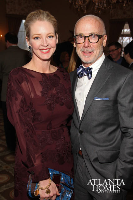 A woman in a burgundy dress and a man in a gray suit with a bow tie pose for a photo.