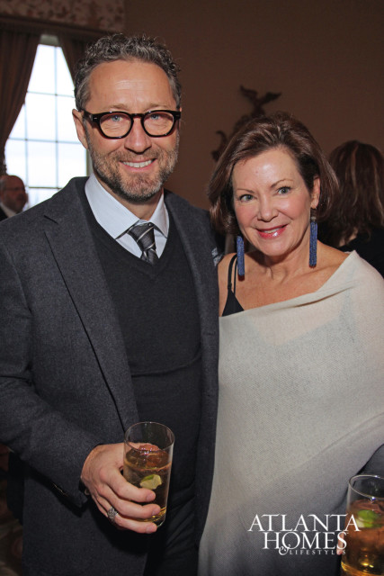 Jeffrey Dungan and Beth Webb pose for a portrait, Dungan holds a drink and wears glasses and a suit, Webb wears a shawl and long earrings.