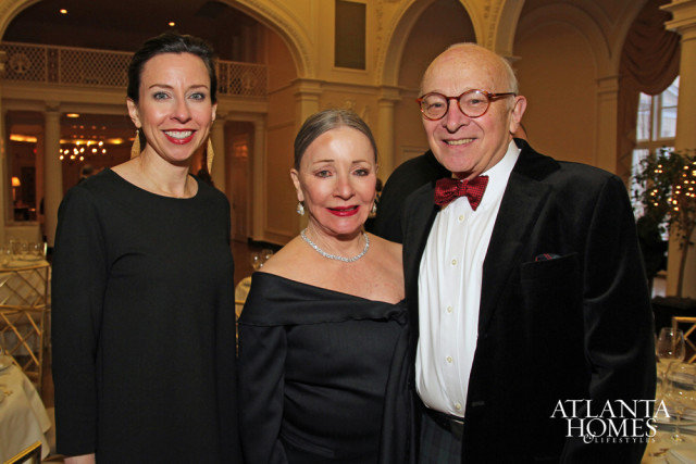 Three people smiling, two women and one man, at an event. The man wears a bow tie and velvet jacket.