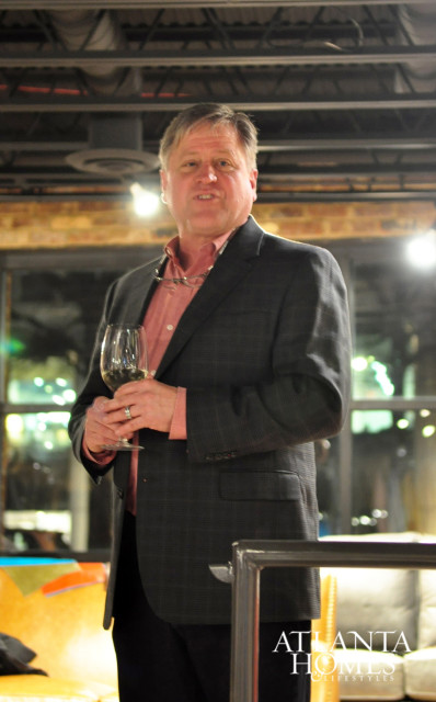 Man in a dark suit and pink shirt holding a glass of white wine. The Atlanta Homes & Lifestyles logo is visible in the lower right corner.