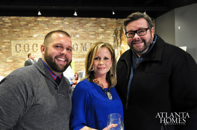Three people smiling at the camera, with a brick wall and a logo for Atlanta Homes & Lifestyles in the background.
