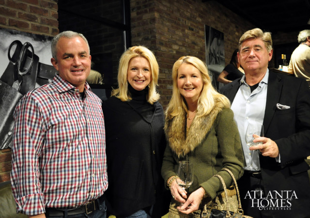 Four people pose for a photo in front of a brick wall. A man in a plaid shirt stands on the left, followed by two women, and a man in a suit on the right holding a wine glass.