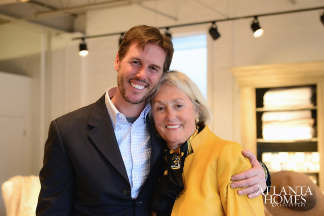 Man in a dark suit and checkered shirt smiles with his arm around a woman in a yellow jacket and black scarf.